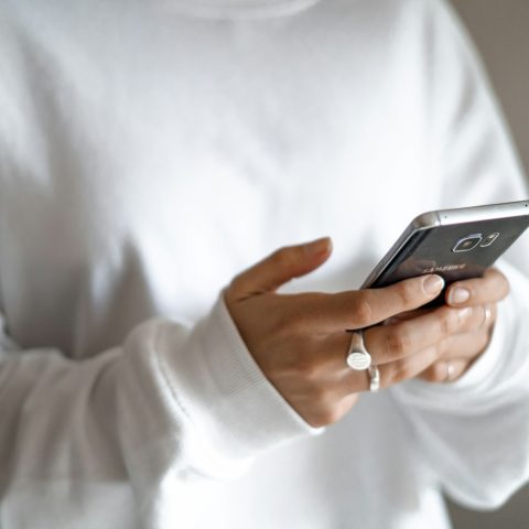 person in white long sleeve shirt holding black smartphone