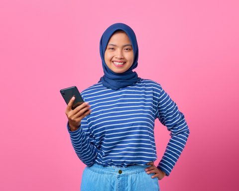 Scholier met smartphone in de klas, terwijl een docent op de achtergrond staat