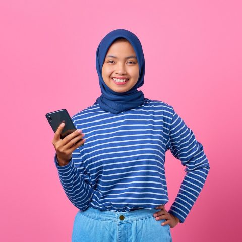 Scholier met smartphone in de klas, terwijl een docent op de achtergrond staat
