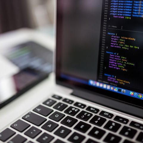Een persoon die achter een laptop code schrijft en beveiligingslekken onderzoekt